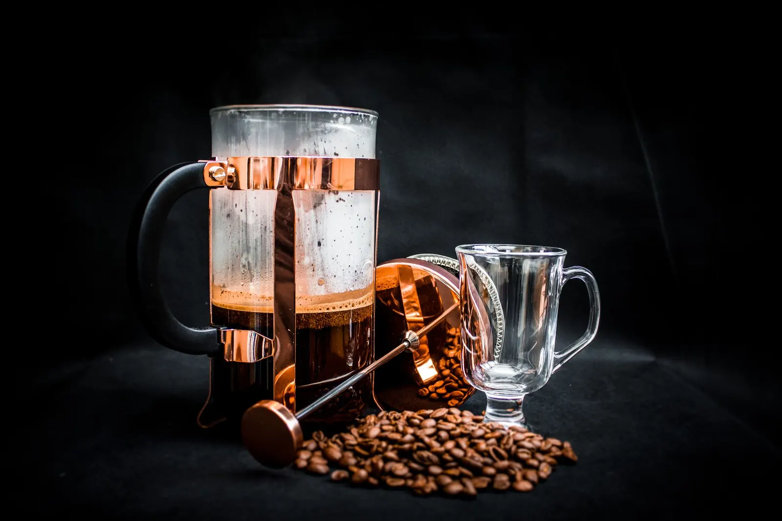 فرنچ‌پرس شیشه‌ای کنار فنجان قهوه روی میز