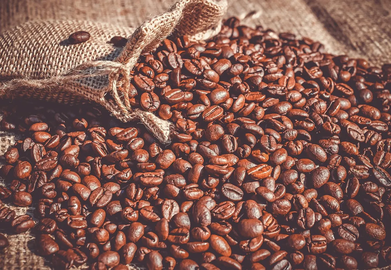 دان قهوه ریخته از کیسه‌ی کتانی روی سطح چوبی