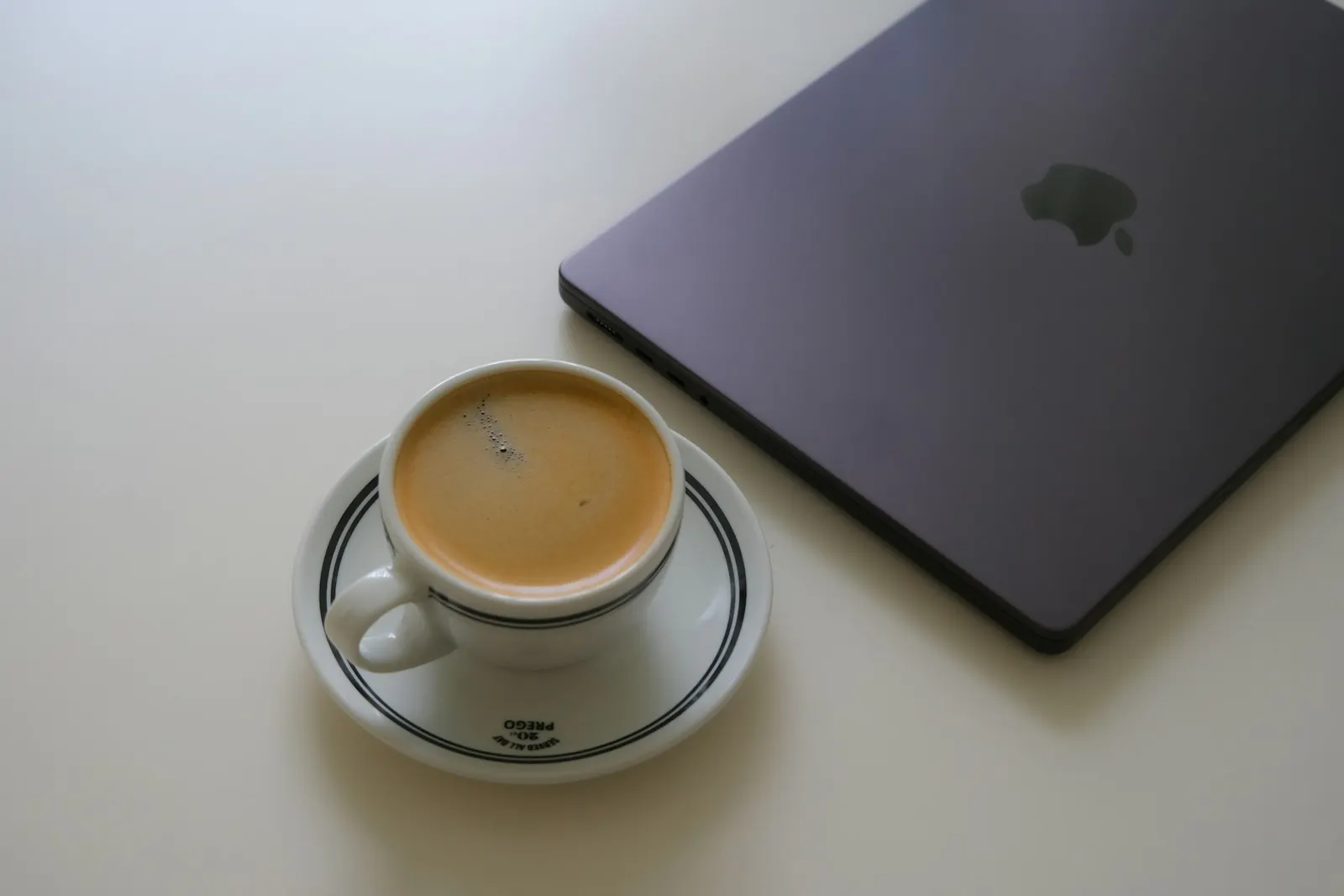 فنجان قهوه کنار لپ‌تاپ روی میز کار سفید